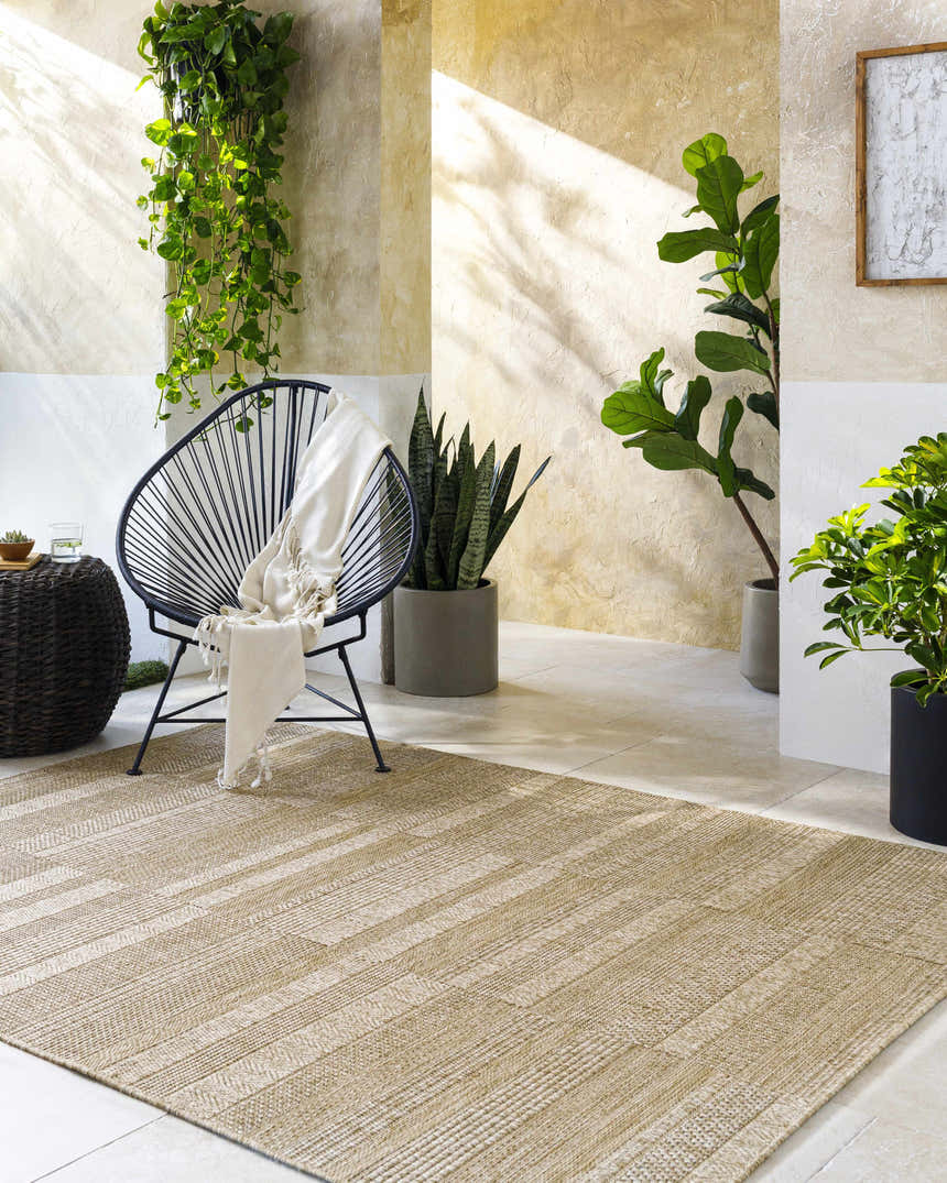 Sunlit patio with Thana Brown Area Rug, black accent chair, and lush green plants creating a relaxing, natural vibe. Roomscene-Rectangle