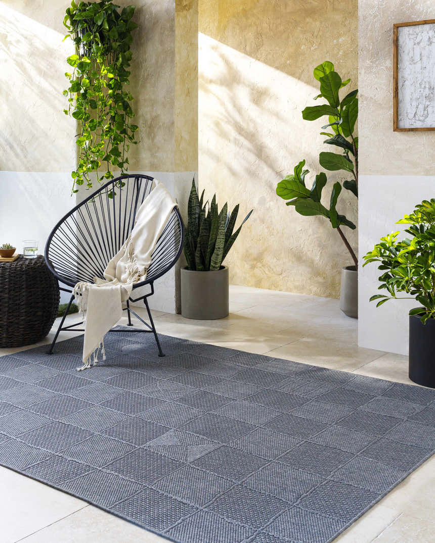 Modern patio scene with Veras Charcoal Area Rug, black chair, and potted plants. Roomscene-Rectangle