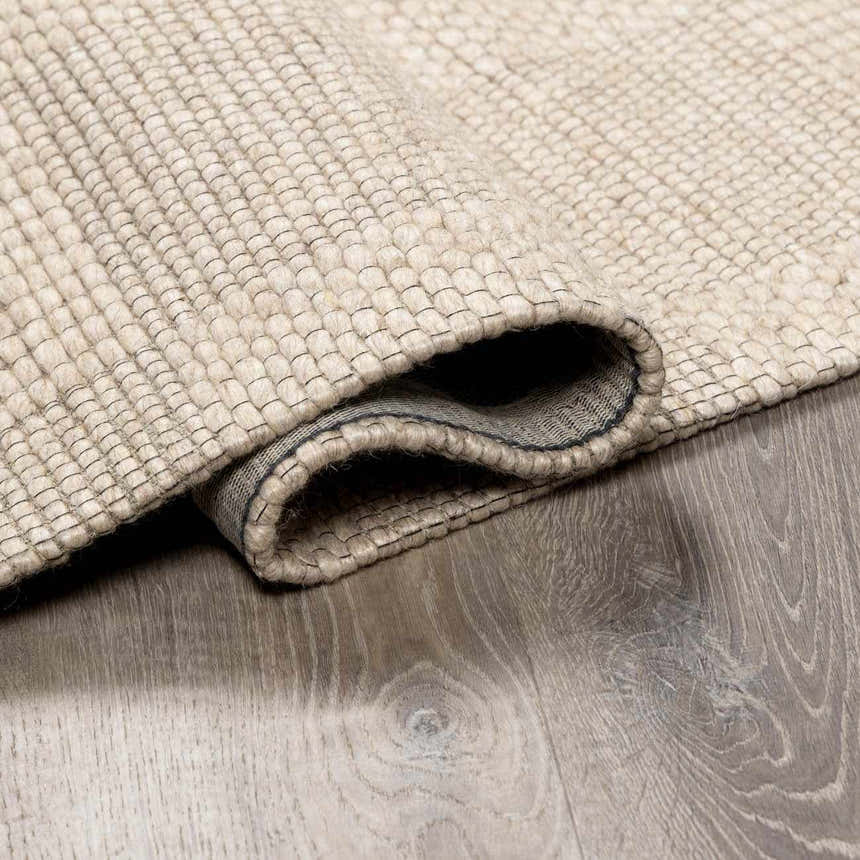 Close-up of the Wolseth Area Rug showing its hand woven texture, off white color, and durable wool and polyester material. Fold