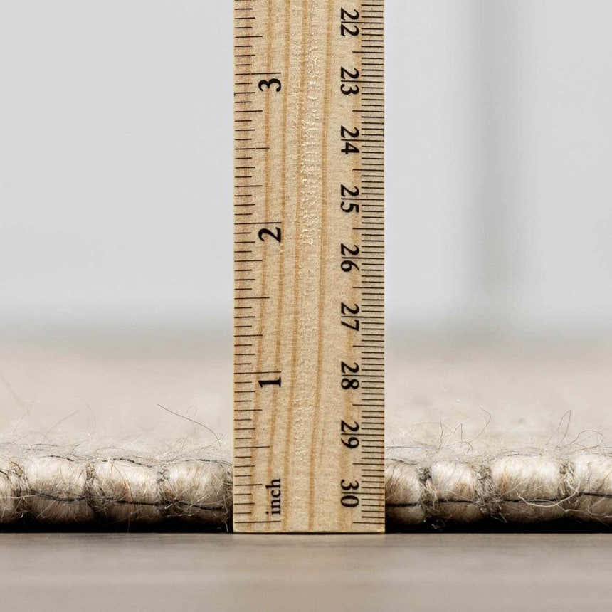 Close-up of the Wolseth Area Rug showing the pile height with a ruler. Off white wool and polyester texture. Pile