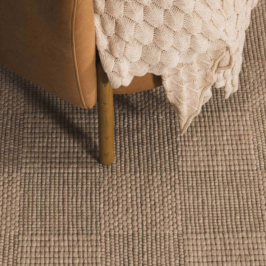 Close-up of the Wolseth Area Rug showing its ivory woven texture next to a tan chair and a cozy knit blanket. Roomscene-Rectangle
