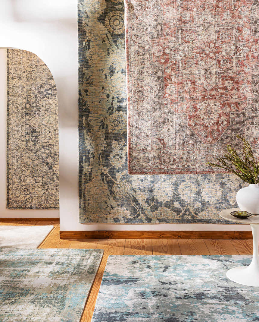 Dunmor Area Rug display: Brick red, charcoal, and cream Persian-style rugs hanging on a white wall above a light wood floor. Styleshot