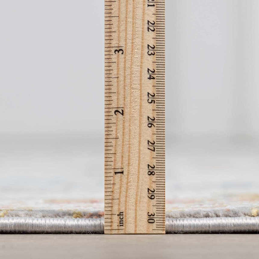 Close-up of Witheridge rug pile height, showing gray, light beige, peach, and mustard colors with a ruler for scale. Pile
