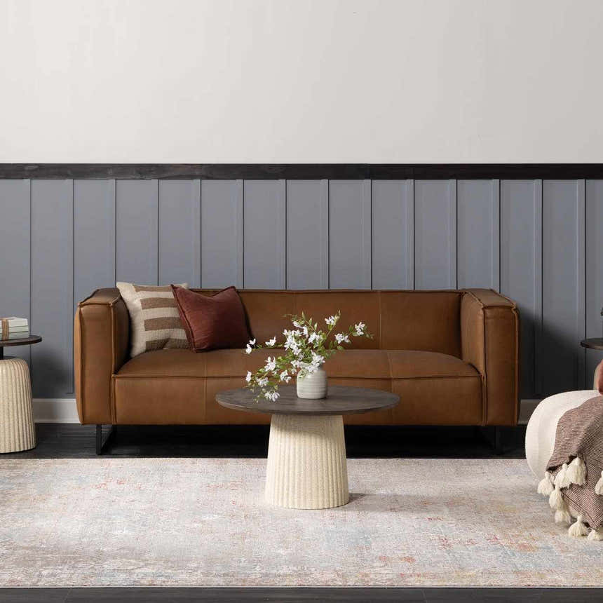 Living room scene with a brown leather sofa and the Witheridge Area Rug in blue, pink, and gray tones. Roomscene-Rectangle