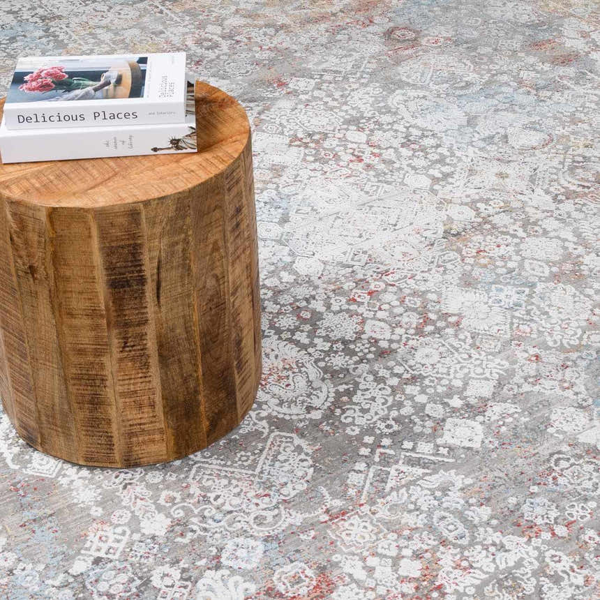 Close-up of the Witheridge Area Rug showing its gray, white, and red traditional pattern next to a wood side table. Styleshot