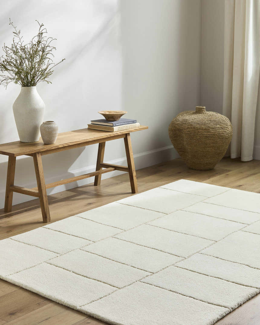 Neutral room scene with a light beige Xylia wool rug, wood bench, vases, and woven basket for a minimalist aesthetic. Roomscene-Rectangle
