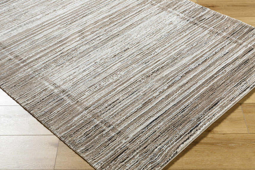 Close-up of Ainhoa Luxe Thick Area Rug. Contemporary style rug in black, ivory, peach, and tan on wood floor. Corner
