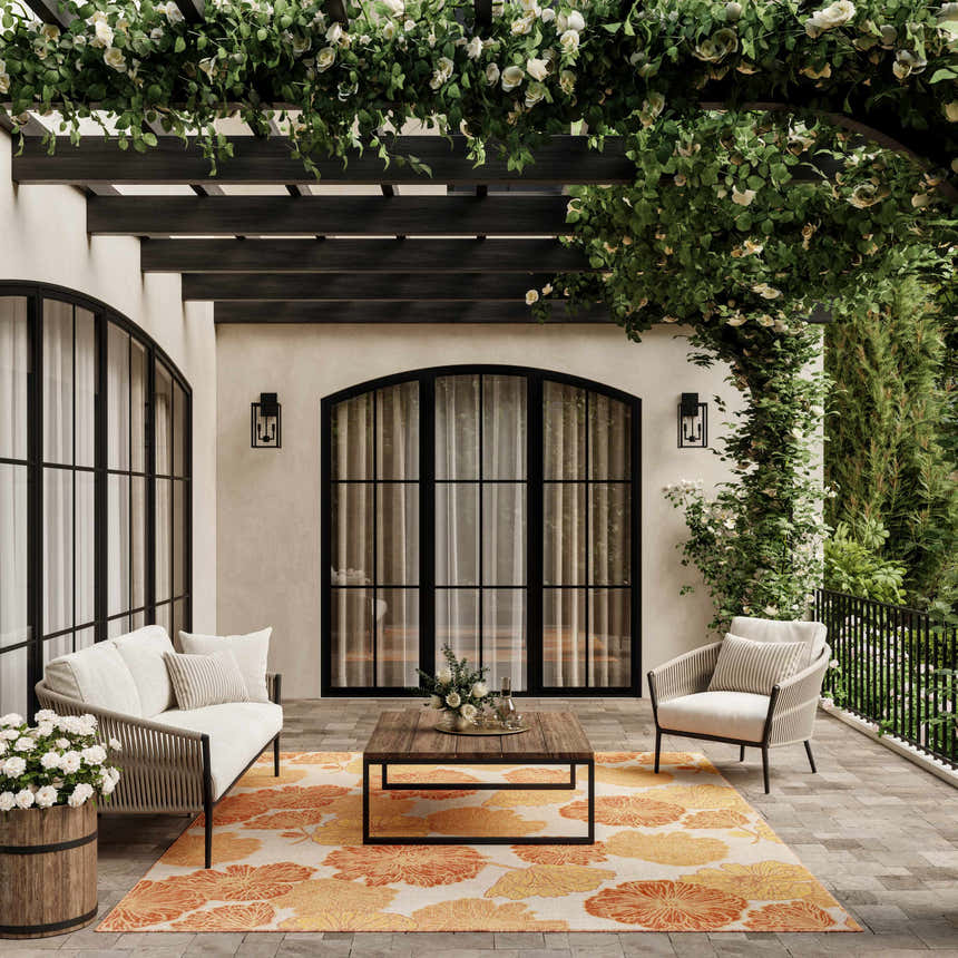 Outdoor patio scene with a Nourison Garden Oasis Coral Tropical Area Rug, sofa, chair, and floral pergola.