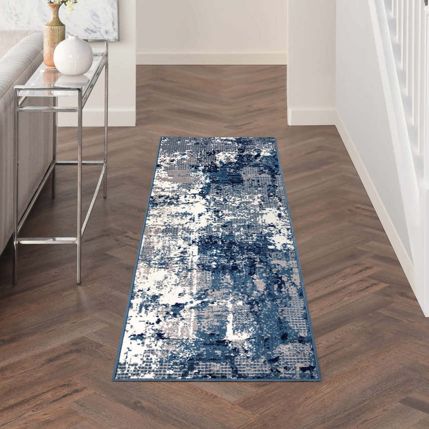 Hallway scene with a Nourison Grafix Navy Blue rug on herringbone wood floors, next to a glass console table.