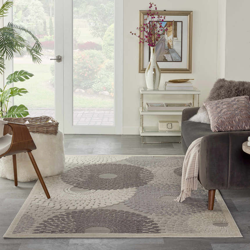 Living room scene with a grey sofa and Nourison Graphic Illusions Grey Mid-Century Modern rug with a large floral pattern.
