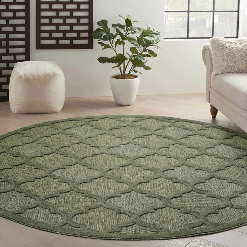 Living room scene with a round Nourison Easy Care Green Modern Area Rug, sofa, ottoman, and plant.