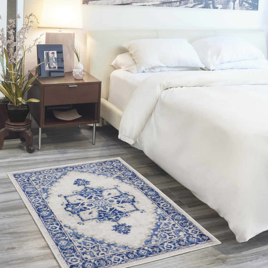 Bedroom scene with Nourison Whimsicle Ivory Blue Farmhouse rug, white bedding, and wood nightstand.