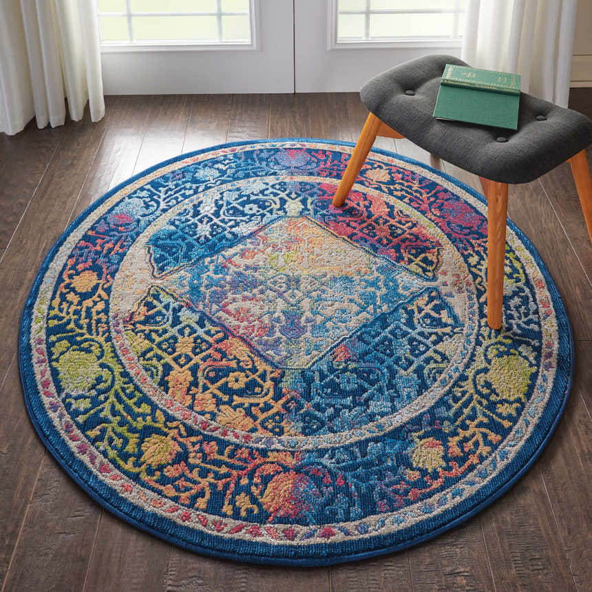 Round Nourison Ankara Global rug in a room with wood floors, a stool, and soft white curtains. Blue multicolor bohemian pattern.