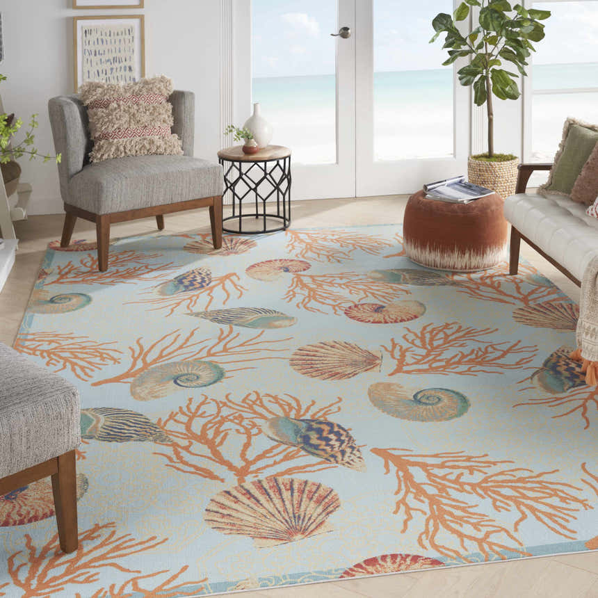 Coastal living room with Waverly Sun N' Shade Light Blue rug, seashell and coral pattern, beach view.