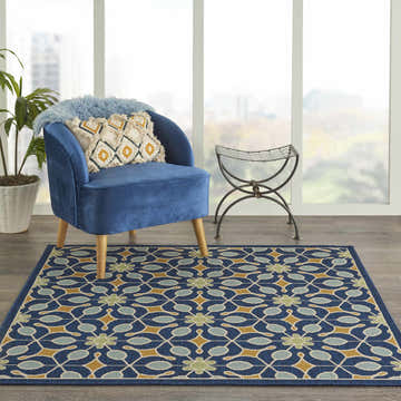 Living room scene with blue chair and Nourison Caribbean Navy Mid-Century Modern area rug with floral geometric pattern.