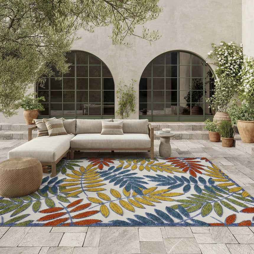 Outdoor patio with sofa and Nourison Aloha Ivory Multicolor Tropical Area Rug with a colorful leaf pattern.