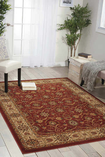 Living room scene with a brick red Nourison Persian Crown rug, white chair and ottoman, and light wood floors.