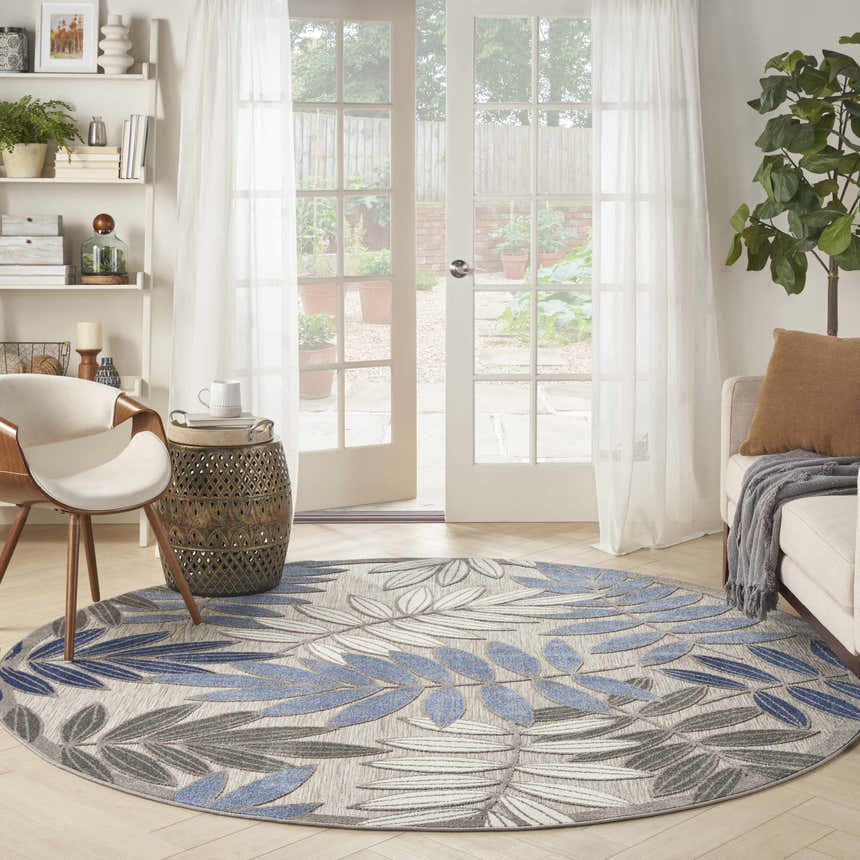Living room scene with a round Nourison Aloha Grey Blue Tropical Area Rug, chair, and garden view.