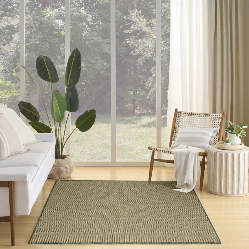 Living room with a Nourison Courtyard Green Modern Area Rug, white sofa, wood chair, and large window with a view of greenery.