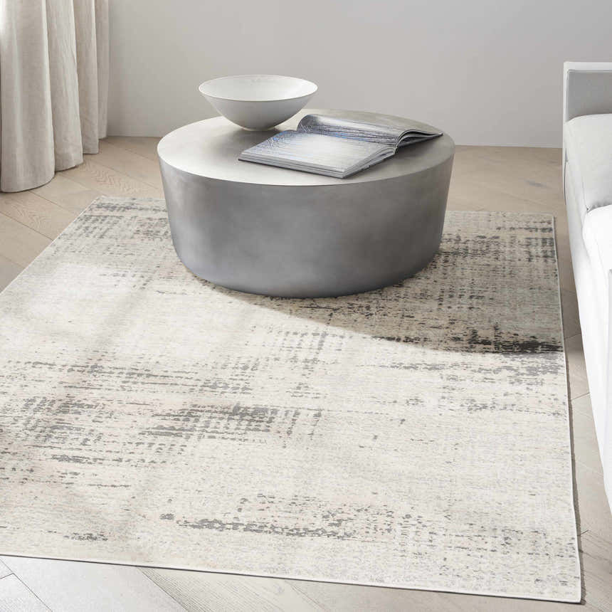 Modern living room scene with a Calvin Klein CK950 Rush Ivory Beige rug under a round concrete coffee table.