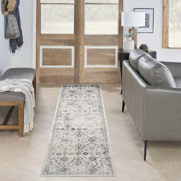 Entryway with a Nourison Astra Ivory Blue Vintage rug, gray leather sofa, wood door, and herringbone floors.