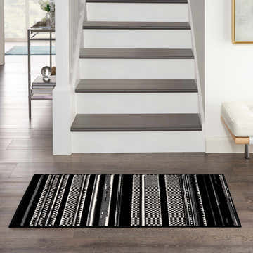 Entryway with Nourison Grafix Black White Modern Indoor Area Rug, stairs, wood floor, and white bench.