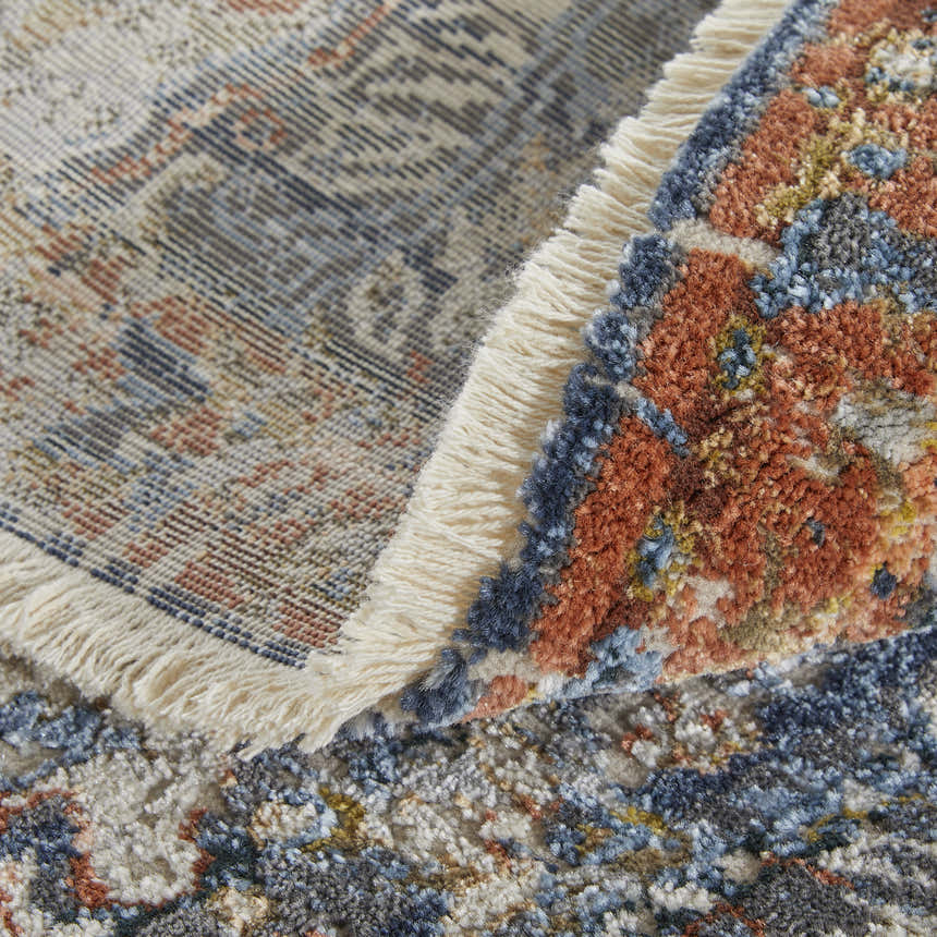 Close-up of the Feizy Kaia rug showing its blue, orange, and ivory floral pattern and fringe detail. Fold