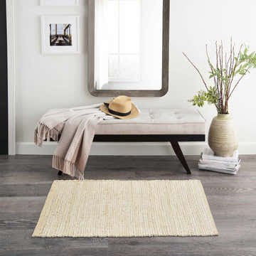 Entryway scene with a Nourison Natural Jute Ivory rug, bench with throw, mirror, and vase with greenery. Farmhouse style.