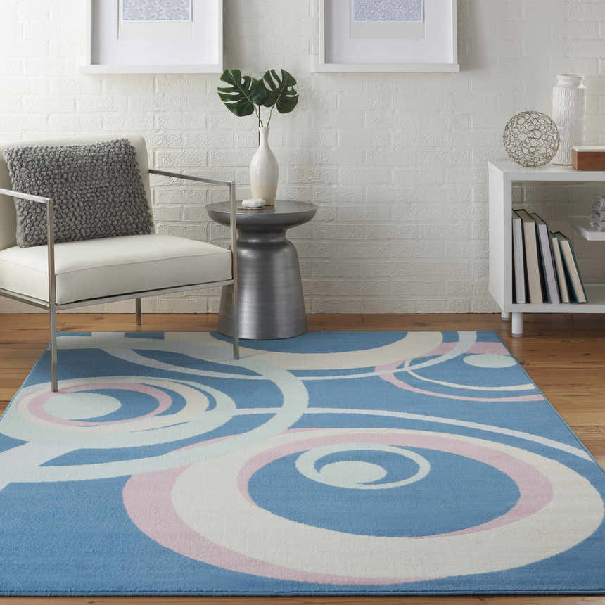 Eclectic living room with a blue Nourison Grafix rug featuring a white and pink swirl pattern. Modern chair and white brick wall.