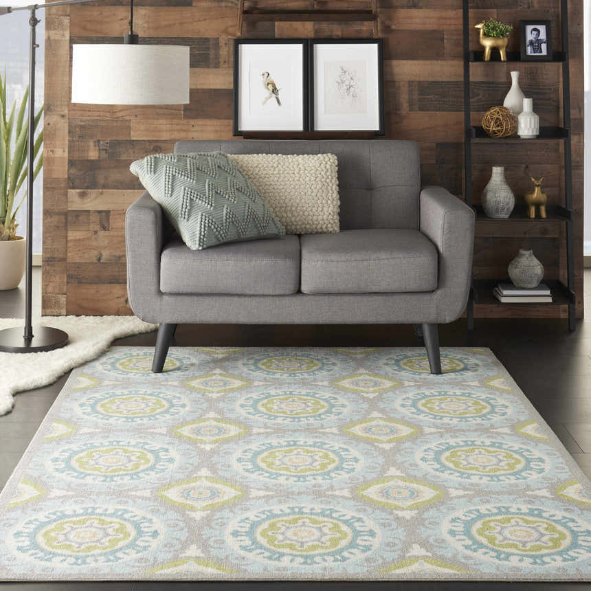 Living room scene with a Waverly Sun N' Shade Jade rug, gray loveseat, wood wall, and coastal decor.