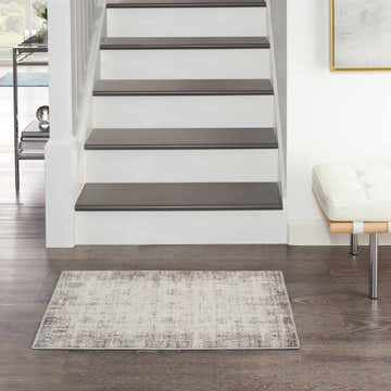Entryway with white stairs and a Nourison Elation Ivory Grey rug on dark wood floors. Modern bench and art.