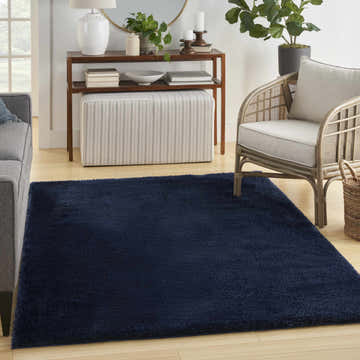 Living room scene with a Nourison Pacific Shag Navy area rug, gray sofa, woven chair, and wood accents.
