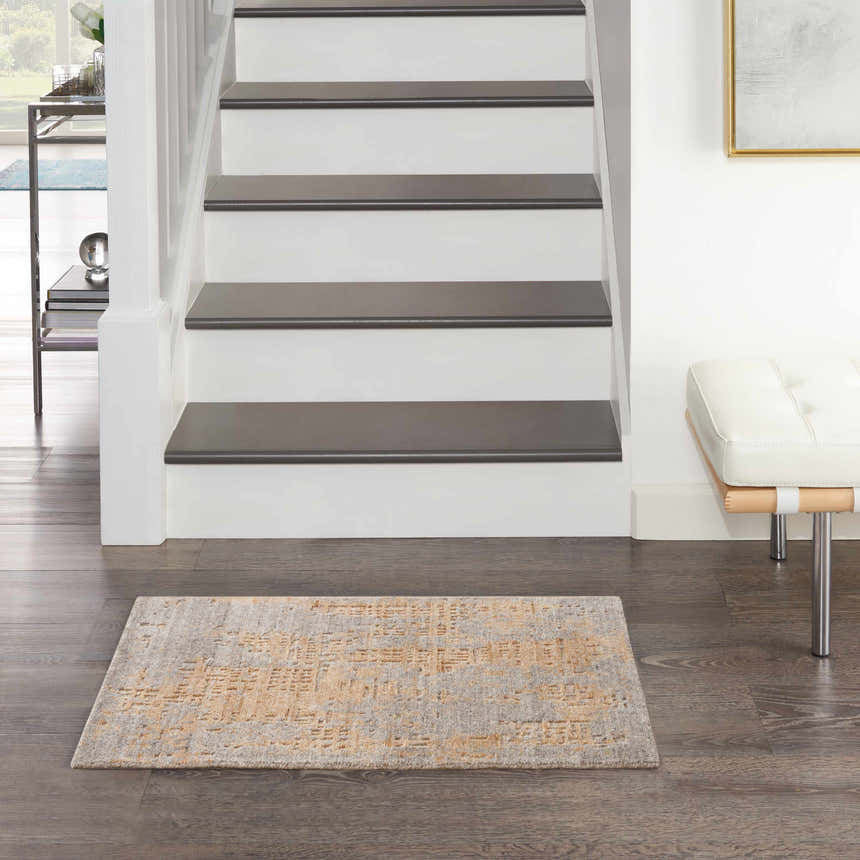 Entryway scene with Nourison Harmony Grey Gold rug, dark wood floors, stairs, and a white leather bench.