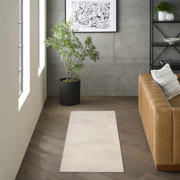 Modern living room with a DKNY Central Park West Beige runner rug, tan leather sofa, and potted tree.