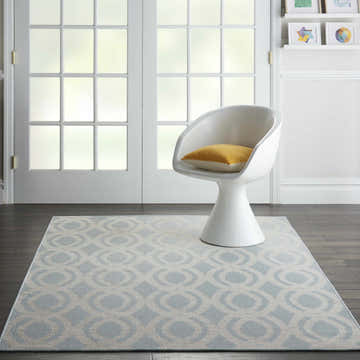 Living room scene with Nourison Aruba Light Blue Cream Beach Area Rug, white chair, wood floors, and natural light.