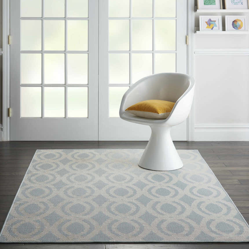 Living room scene with Nourison Aruba Light Blue Cream Beach Area Rug, white chair, wood floors, and natural light.