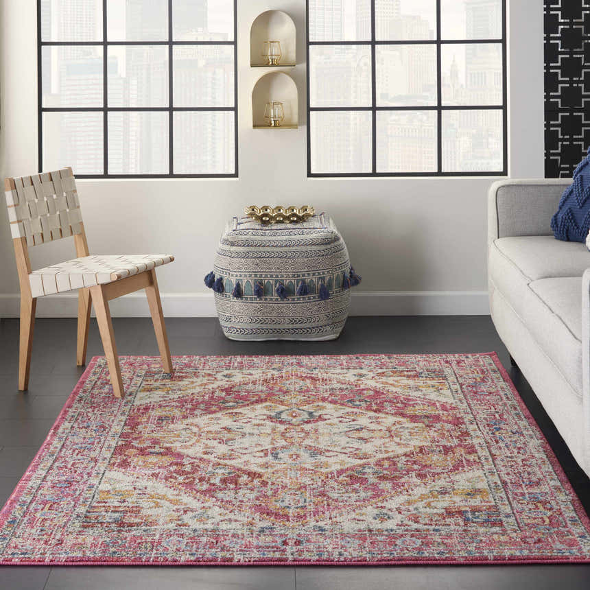 Living room scene with a Nourison Passion Ivory Pink Bohemian rug, light gray sofa, woven chair, and patterned ottoman.