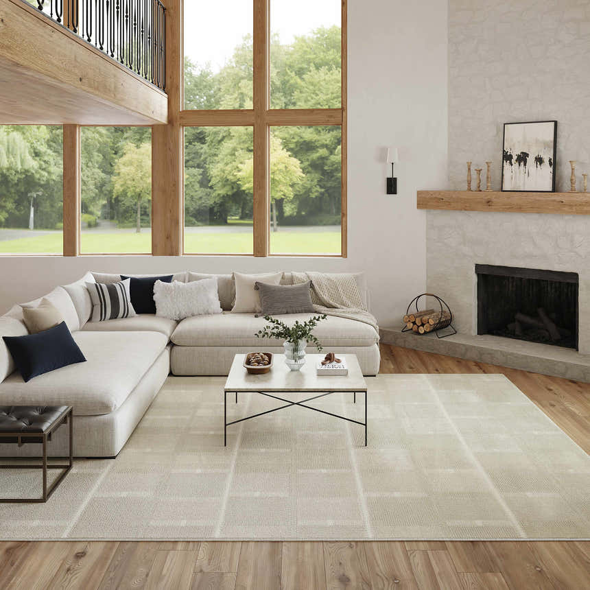 Modern living room with a Nourison Nordic Ivory Beige rug, sectional sofa, stone fireplace, and large windows.