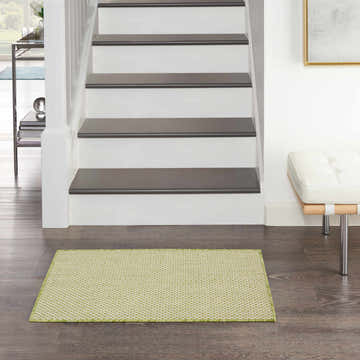 Entryway scene with Nourison Courtyard Ivory Green rug on dark wood floor, white stairs, and a white leather bench.