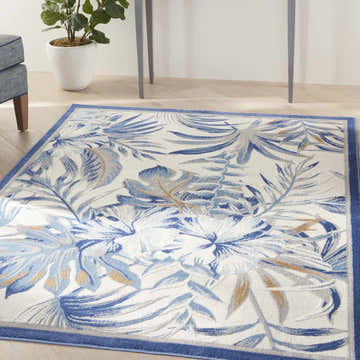 Living room scene with a Nourison Seaside Ivory Blue Tropical rug featuring a blue botanical leaf pattern.