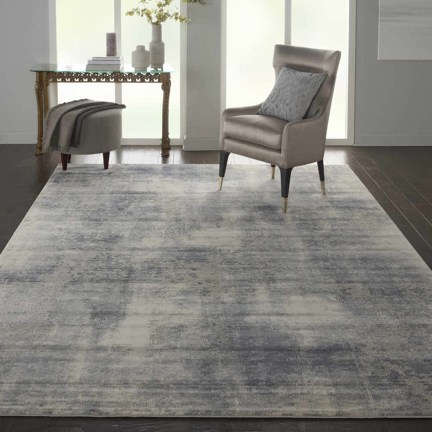 Living room scene with Nourison Rustic Textures Blue Ivory Modern Indoor Area Rug, gray chair, and dark wood floors.