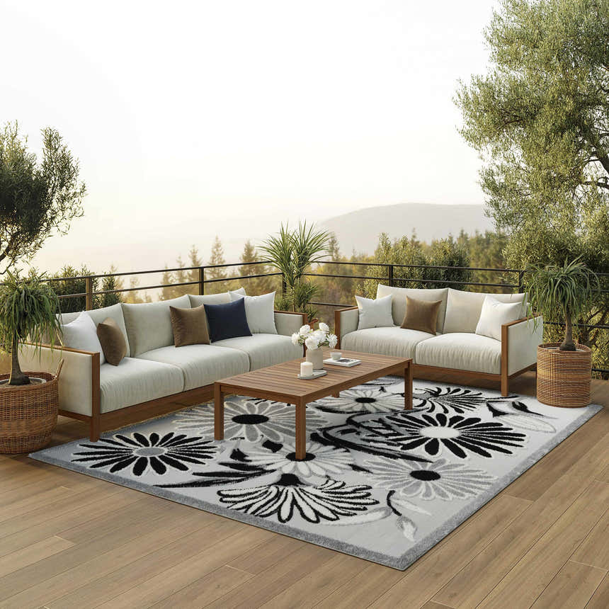 Outdoor patio scene with white sofas, wood table, and Nourison Aloha Black White Outdoor Area Rug.