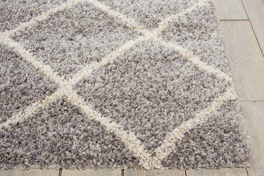 Close-up of the plush Nourison Brisbane Ash Shag rug with a geometric diamond pattern. Soft gray and ivory tones.