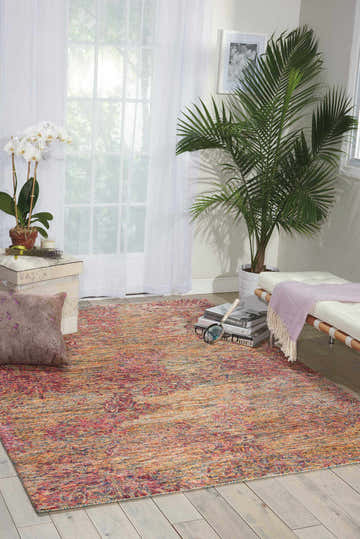 Bright living room with Nourison Gemstone Tourmaline rug in orange, red, and blue. Plants and white furniture accent the space.