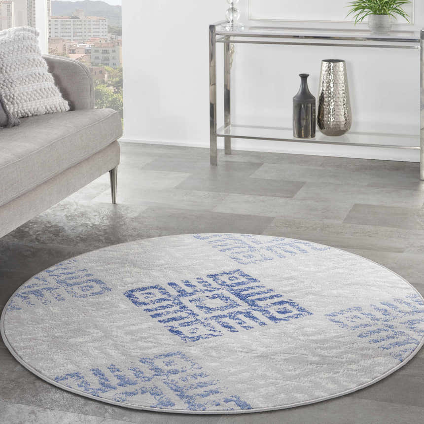 Living room scene with grey sofa and round Nourison Whimsicle Grey Blue rug with a geometric pattern.