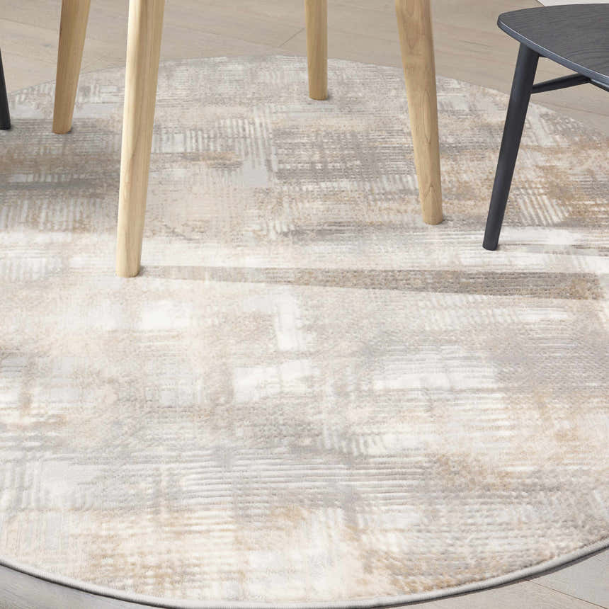 Close-up of a round Calvin Klein CK950 Rush rug in grey and beige with a subtle, modern pattern under a table.