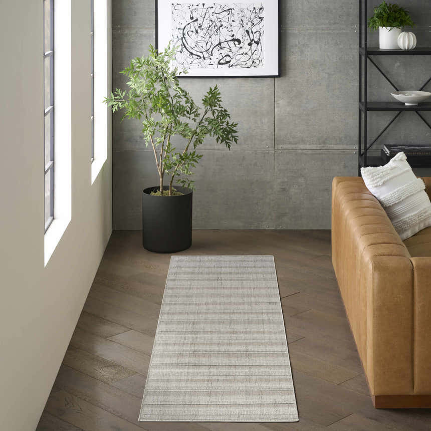 Living room scene with DKNY Pure Multi Weave Grey rug, tan leather sofa, modern art, and plant. Contemporary style.
