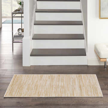 Hallway scene with Nourison Essentials Ivory Gold Outdoor Area Rug on dark wood floors near stairs.