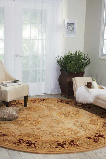 Living room scene with a round, beige Nourison 2000 Persian Indoor Area Rug, chairs, and a plant.