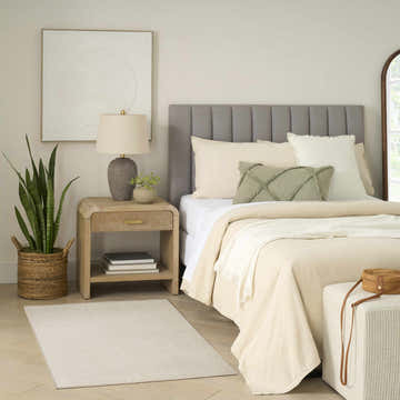 Neutral bedroom scene with a Nourison Charm Ivory rug, wood nightstand, gray headboard, and woven accents.
